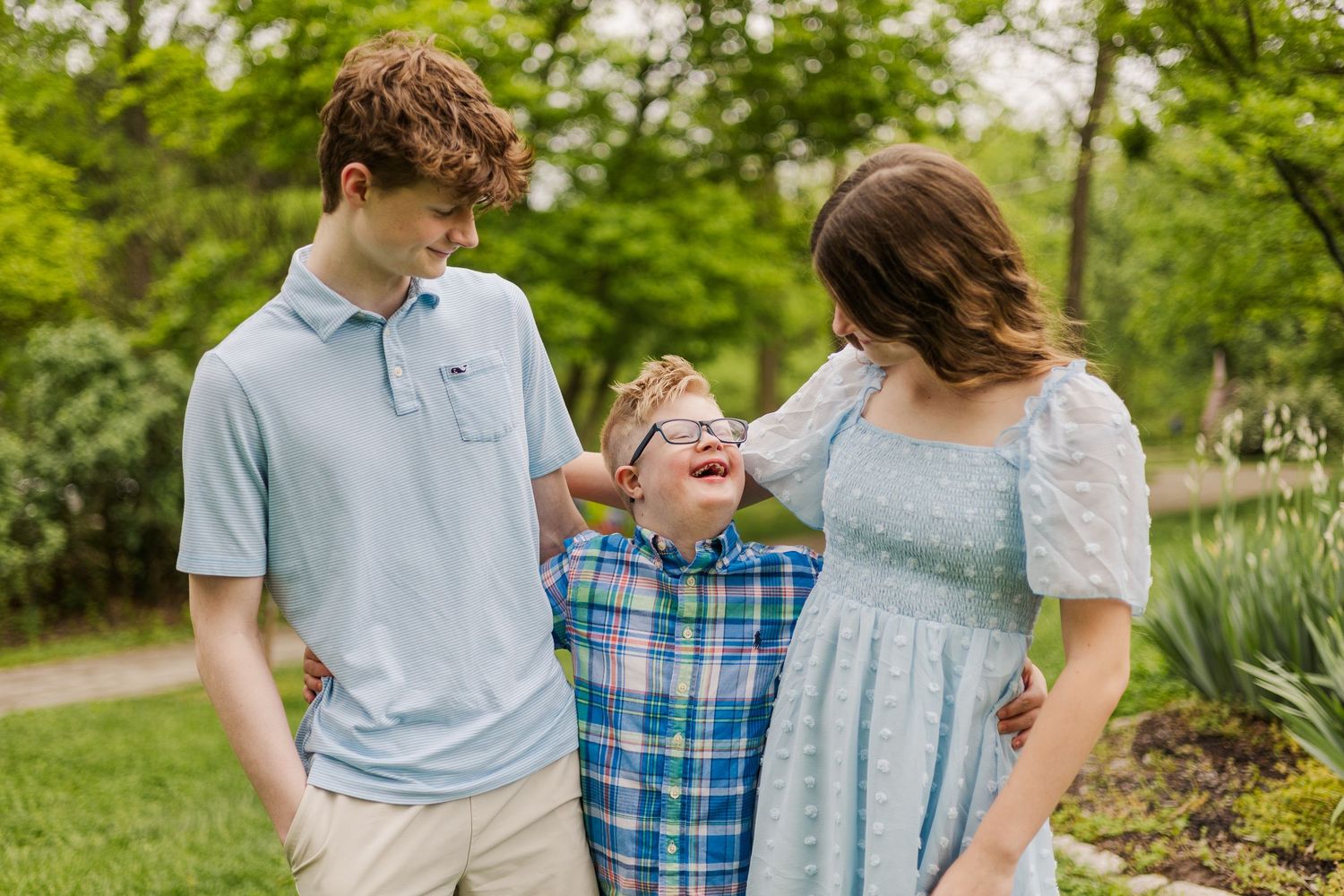 Family wearing coordinated blue and white outfits poses together in a lush garden setting during spring.
