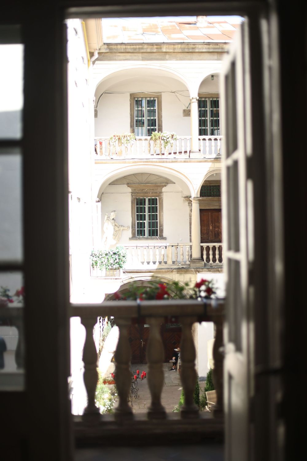View through an open door of a sunlit European courtyard with arched balconies and flowers.