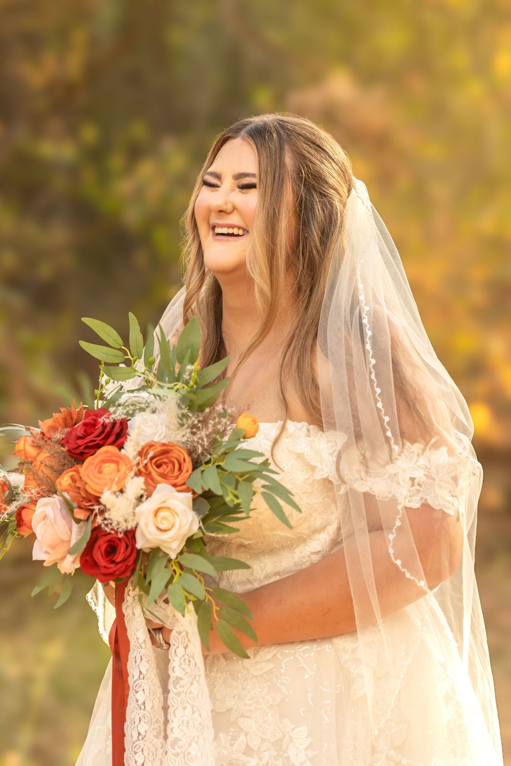 A bride in a white lace gown and veil holds a vibrant autumn bouquet in warm sunlight taken by fresno photographer
