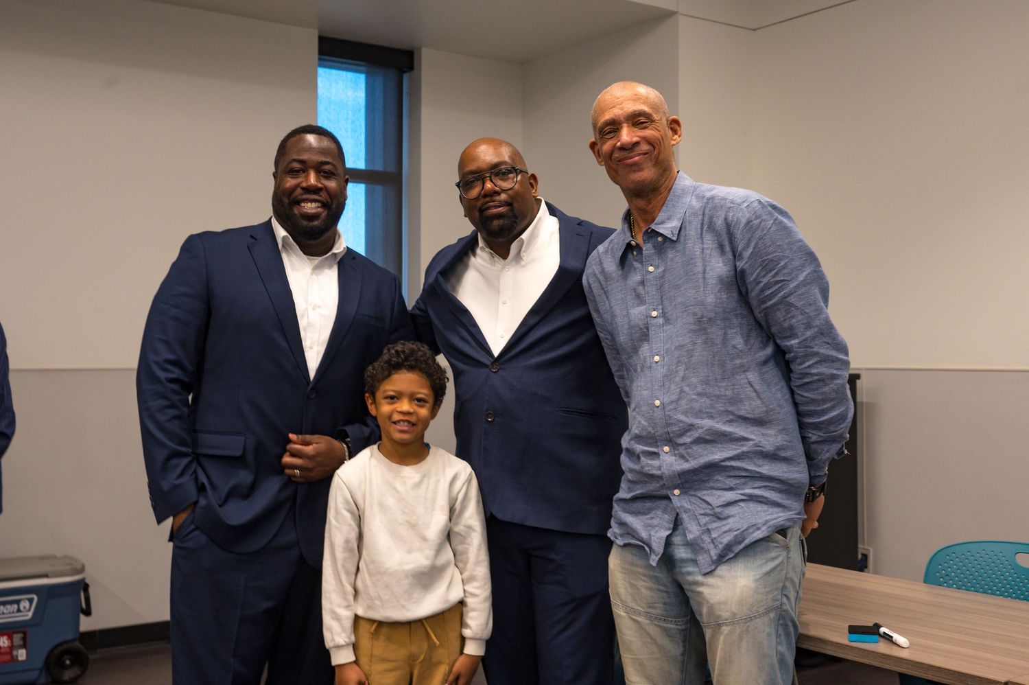 Three men and a small child posing for a friendly group photo in an indoor setting.