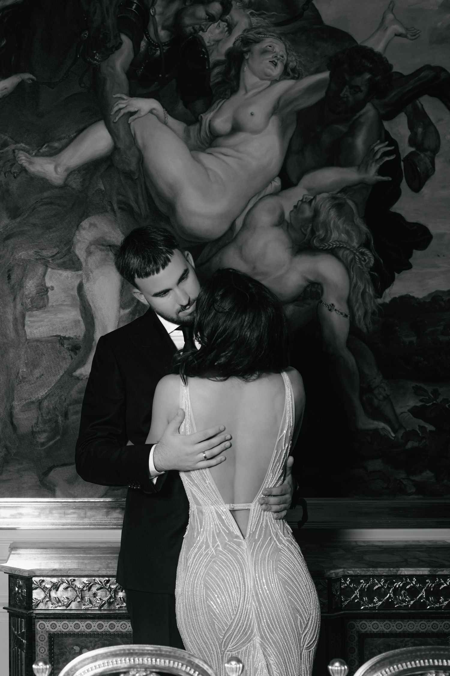 Elegant couple embracing in black and white before a classical baroque painting in ornate interior.