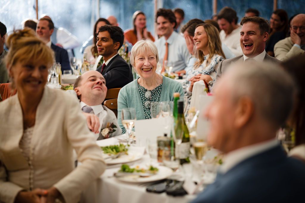 Guests laughing and smiling at a wedding reception dinner table in a marquee tent at Oceanstone Resort