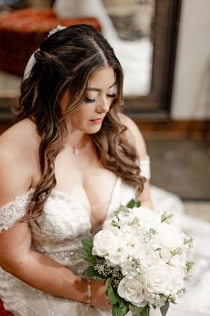 Beautiful bride in off-shoulder lace gown holding white rose bouquet with elegant half-up hairstyle.