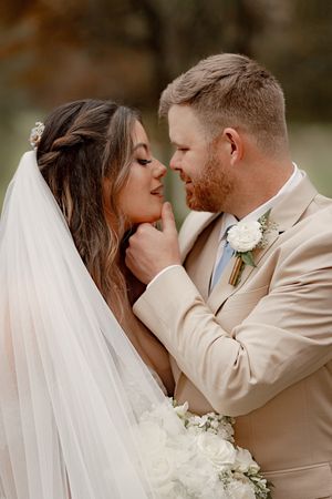 Bride and groom sharing a romantic intimate moment under a wedding veil surrounded by autumn trees.
