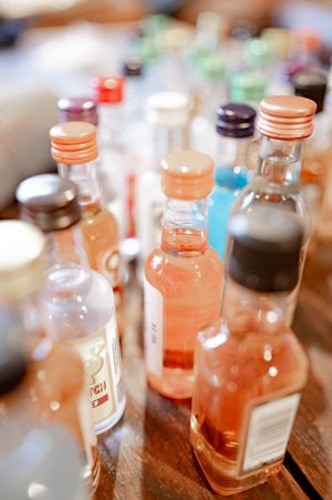 Collection of mini liquor bottles with colorful caps arranged on a wooden table at a wedding reception.