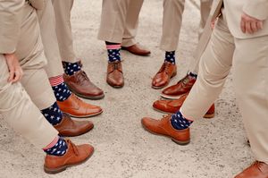 Groomsmen wearing matching American flag socks with brown dress shoes and khaki pants at a wedding.