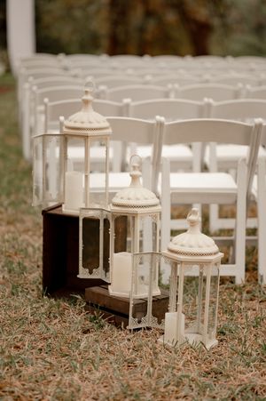 White vintage lanterns on wooden crates line the aisle at an outdoor wedding ceremony.