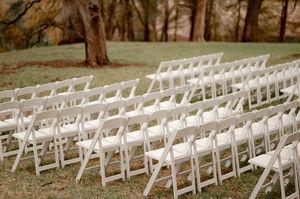 Rows of white folding chairs arranged outdoors on grass for an elegant garden wedding ceremony.