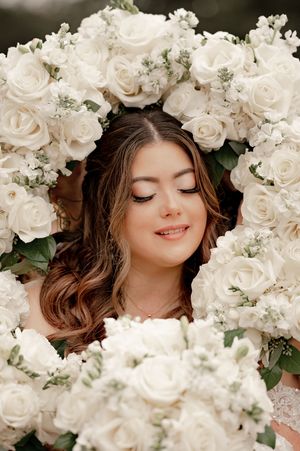 Bride with closed eyes framed by a heart-shaped arrangement of white roses and greenery, bridal portrait.