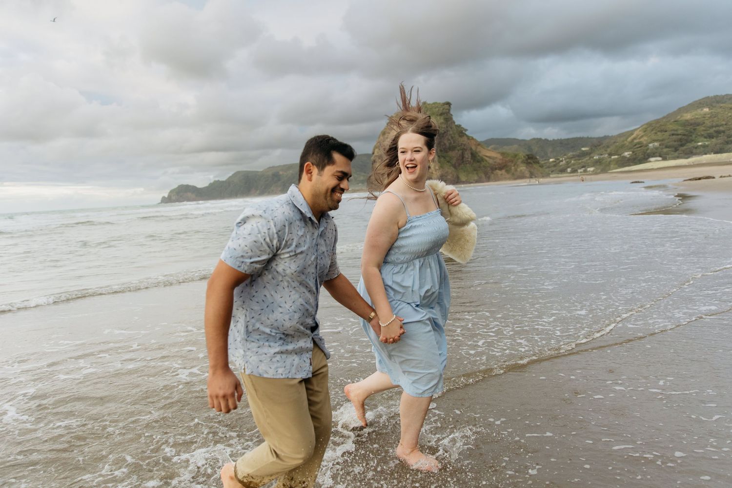 Couple laughing and running during West Auckland beach engagement shoot