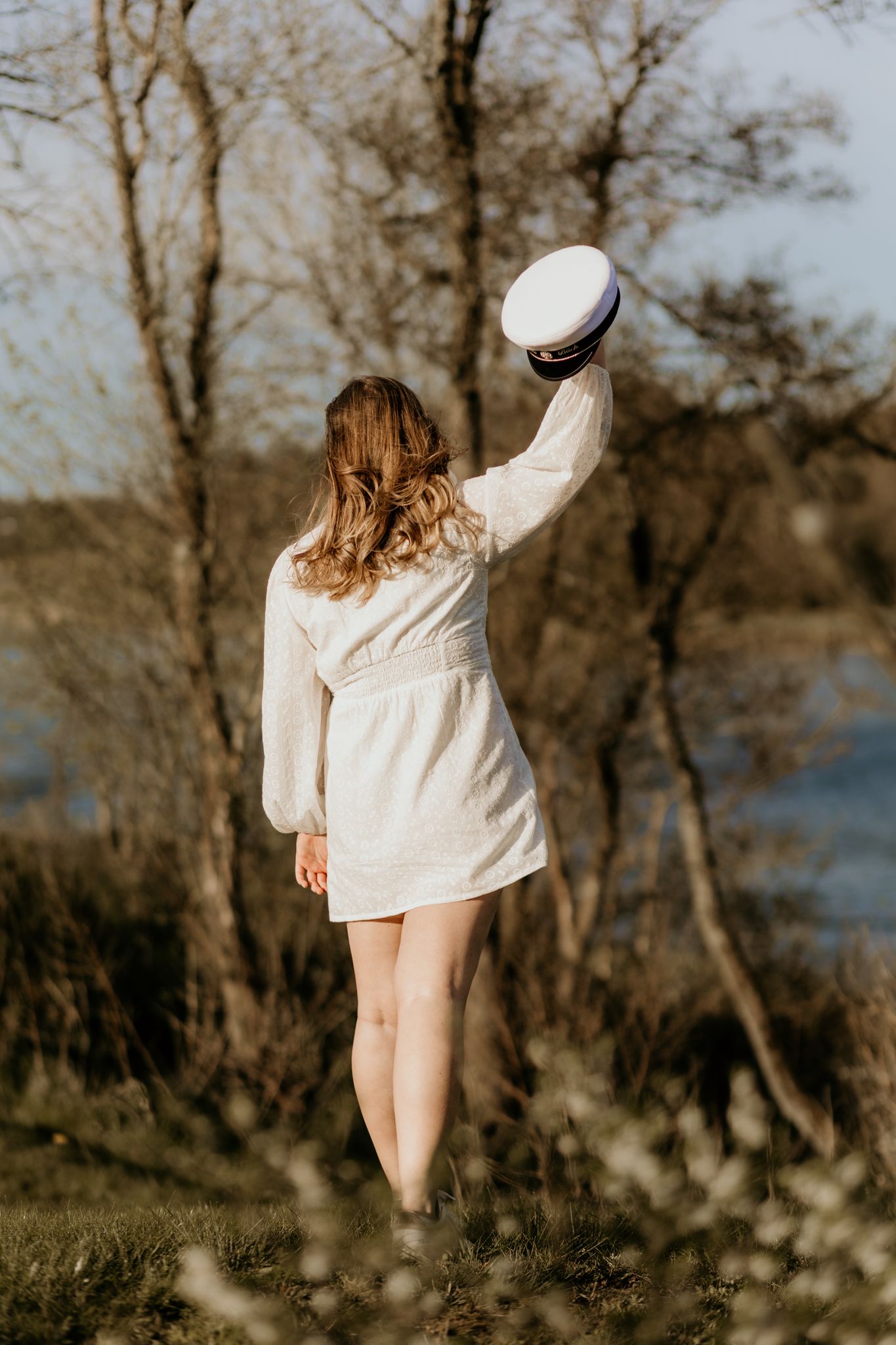 Young girl in white dress standing beside a chestnut horse in a sunlit forest clearing with spring flowers.