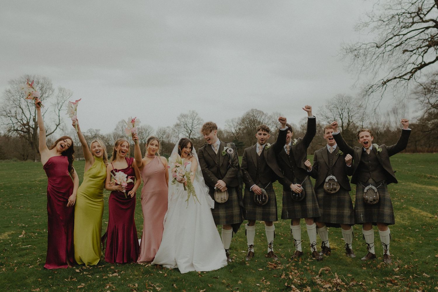 A bride in a white gown and groom in a Scottish kilt share a loving glance outdoors at their wedding.