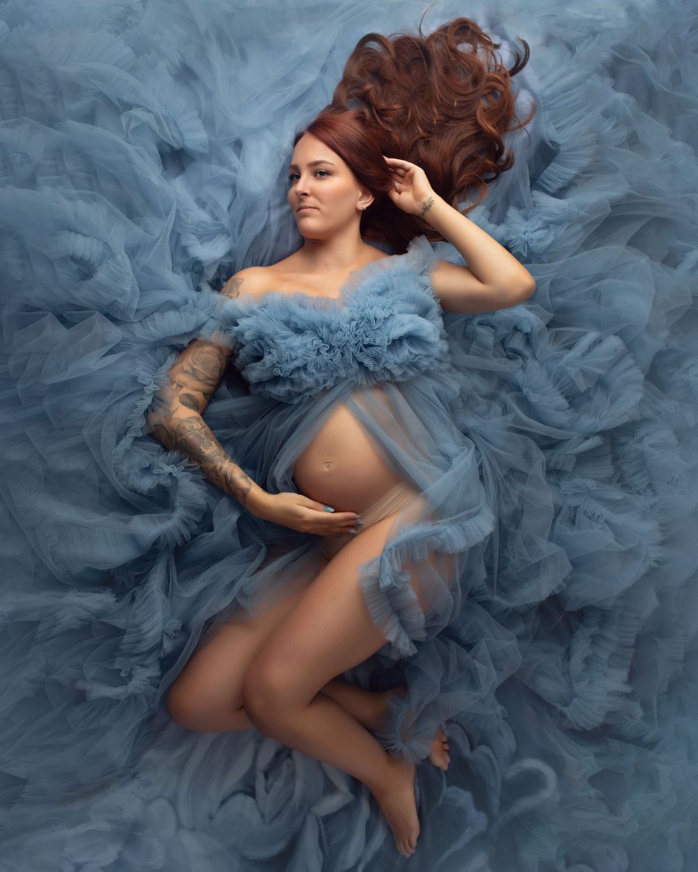 A dreamy maternity photoshoot featuring flowing blue tulle dress with flowing fabric creating an ethereal underwater effect.