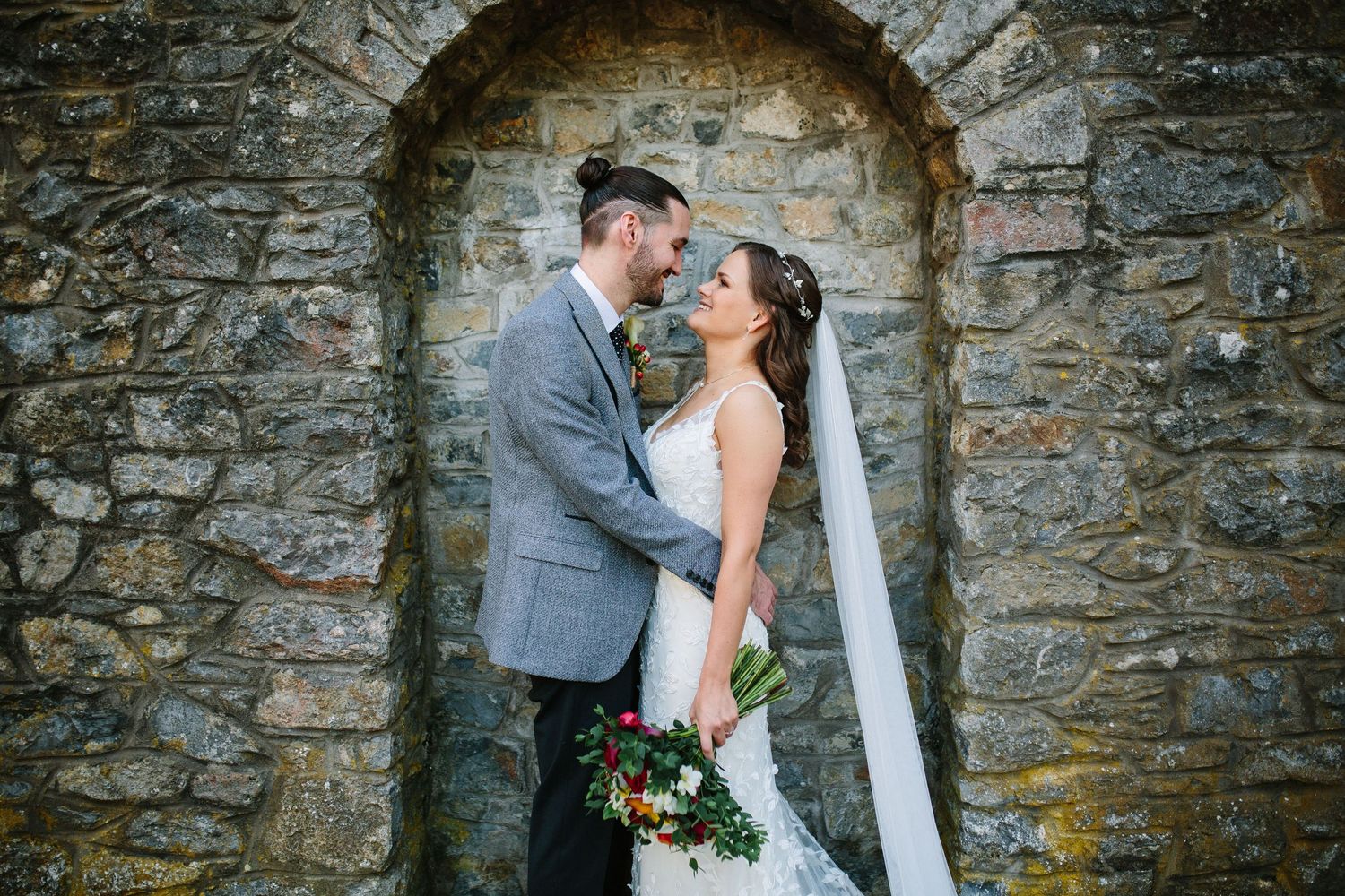 Bride and groom standing before a rustic white barn with red doors on their wedding day.