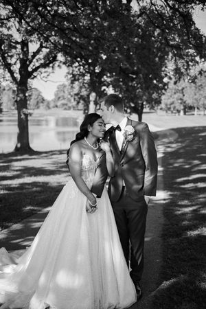 Black and white wedding photo of bride and groom sharing a romantic moment outdoors near a lake surrounded by trees.