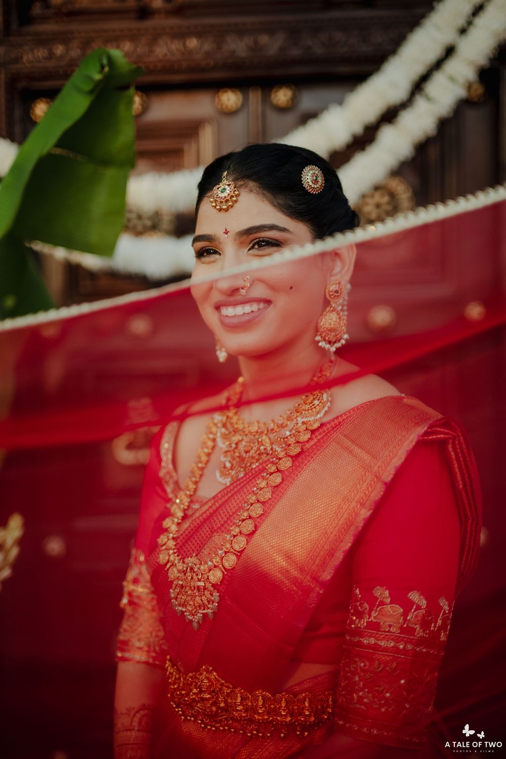 Beautiful Indian bride in red Kanjivaram saree adorned with gold temple jewelry and maang tikka smiling radiantly.