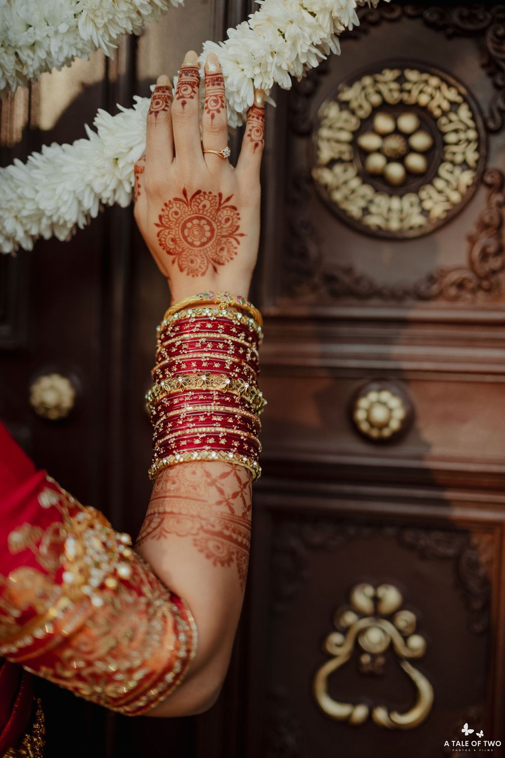 Close-up of bridal hand with intricate henna mehndi design and red and gold bangles at Indian wedding.