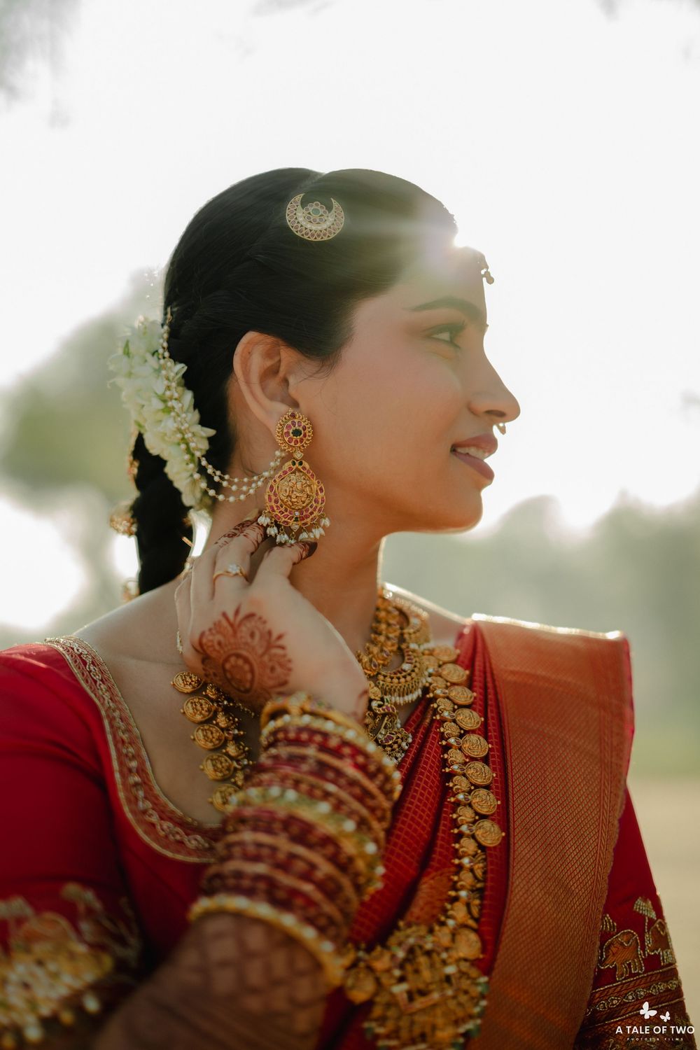 South Indian bride in profile wearing gold chandbali earrings and floral hair accessories.