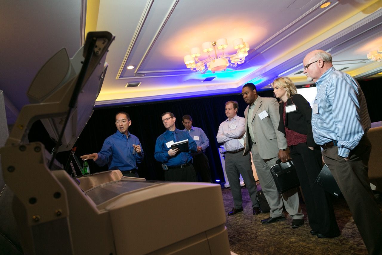Group of professionals gathered around office equipment display at an indoor conference or trade show event at the rosewood mansion