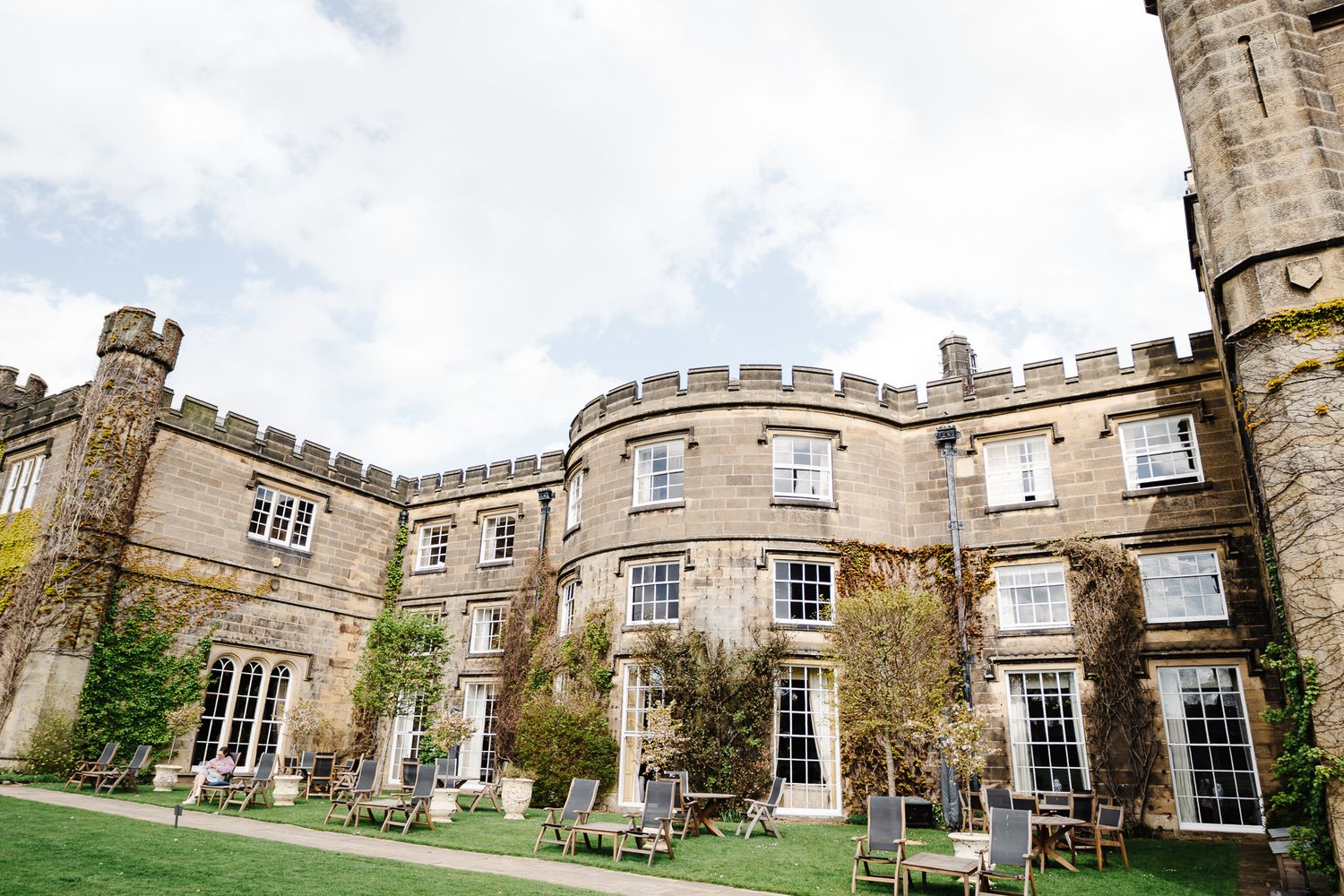 Grand English castle manor with battlements, ivy-covered stone walls, and outdoor seating on manicured lawns.