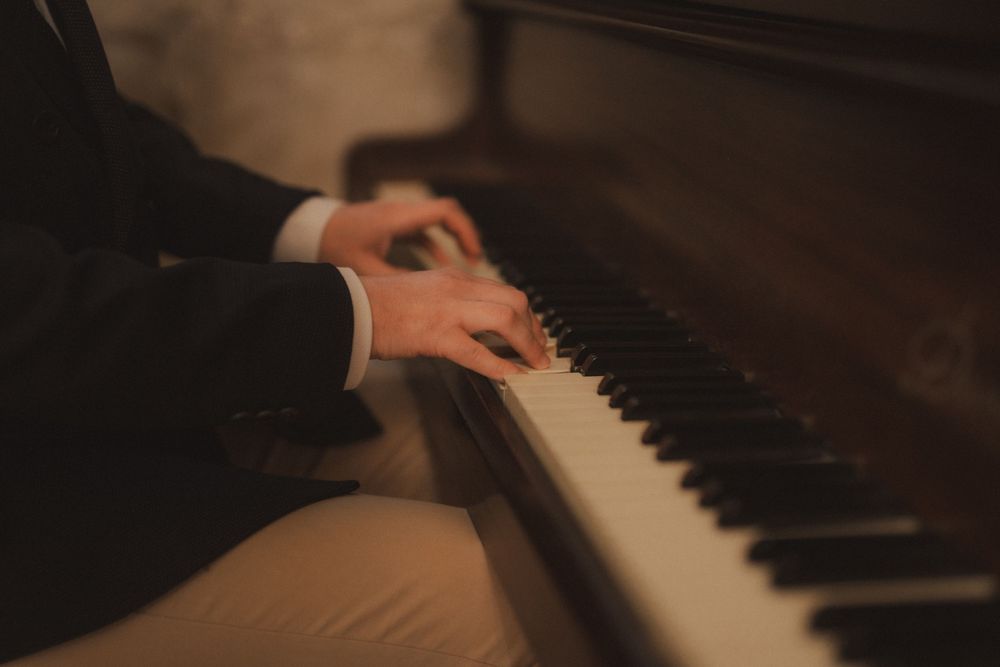 A pianist plays a grand piano, fingers gracefully pressing black and white keys in warm, moody lighting.