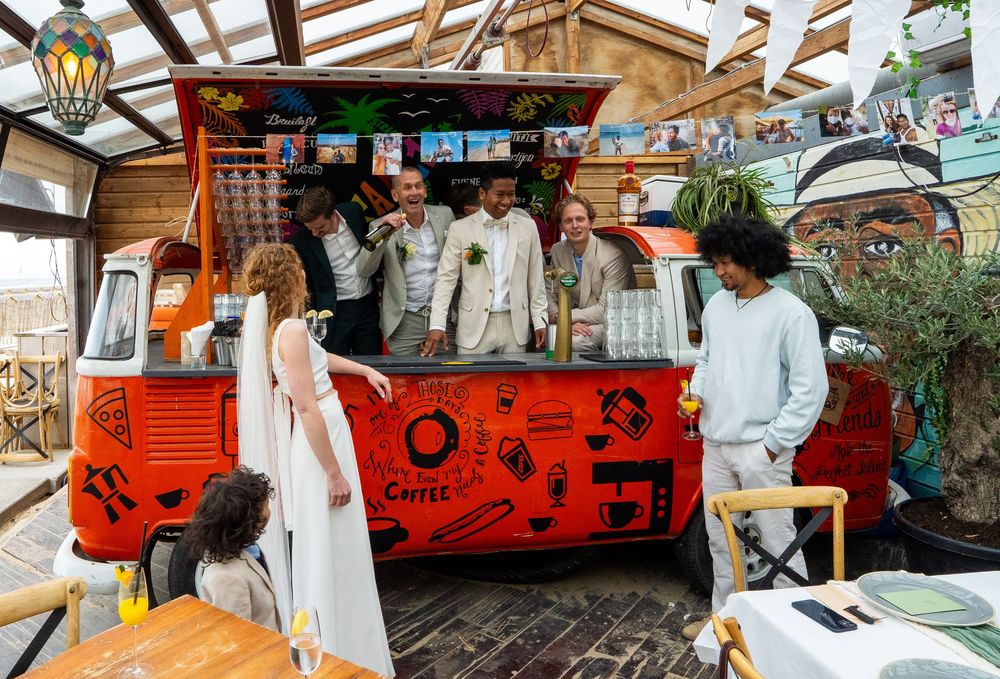Gasten verzamelen zich rond een vintage rode koffiewagen op een buitenlocatie voor een bruiloftsreceptie. award foto door trouwfotograaf