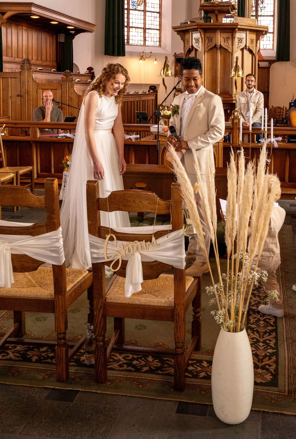 Bruid en bruidegom staan ​​samen bij versierde stoelen in een elegante houten kerk tijdens de huwelijksplechtigheid. christelijke trouw