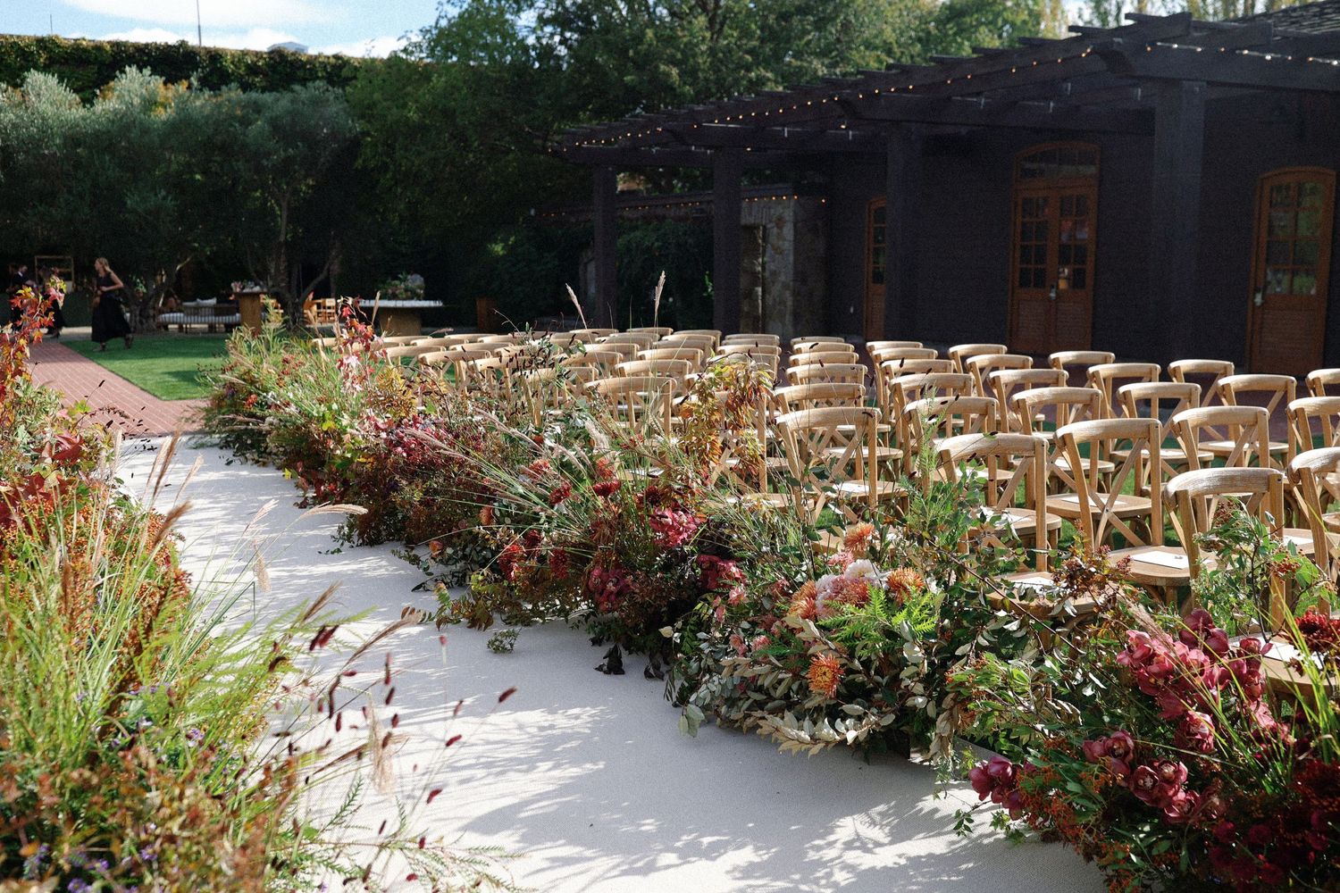 An outdoor wedding ceremony setup with white chairs and colorful floral aisle decorations.