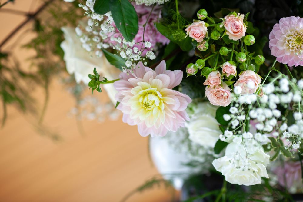 Elegant floral arrangement featuring pink dahlias, spray roses, green berries, and white baby's breath in a soft pastel bouquet.