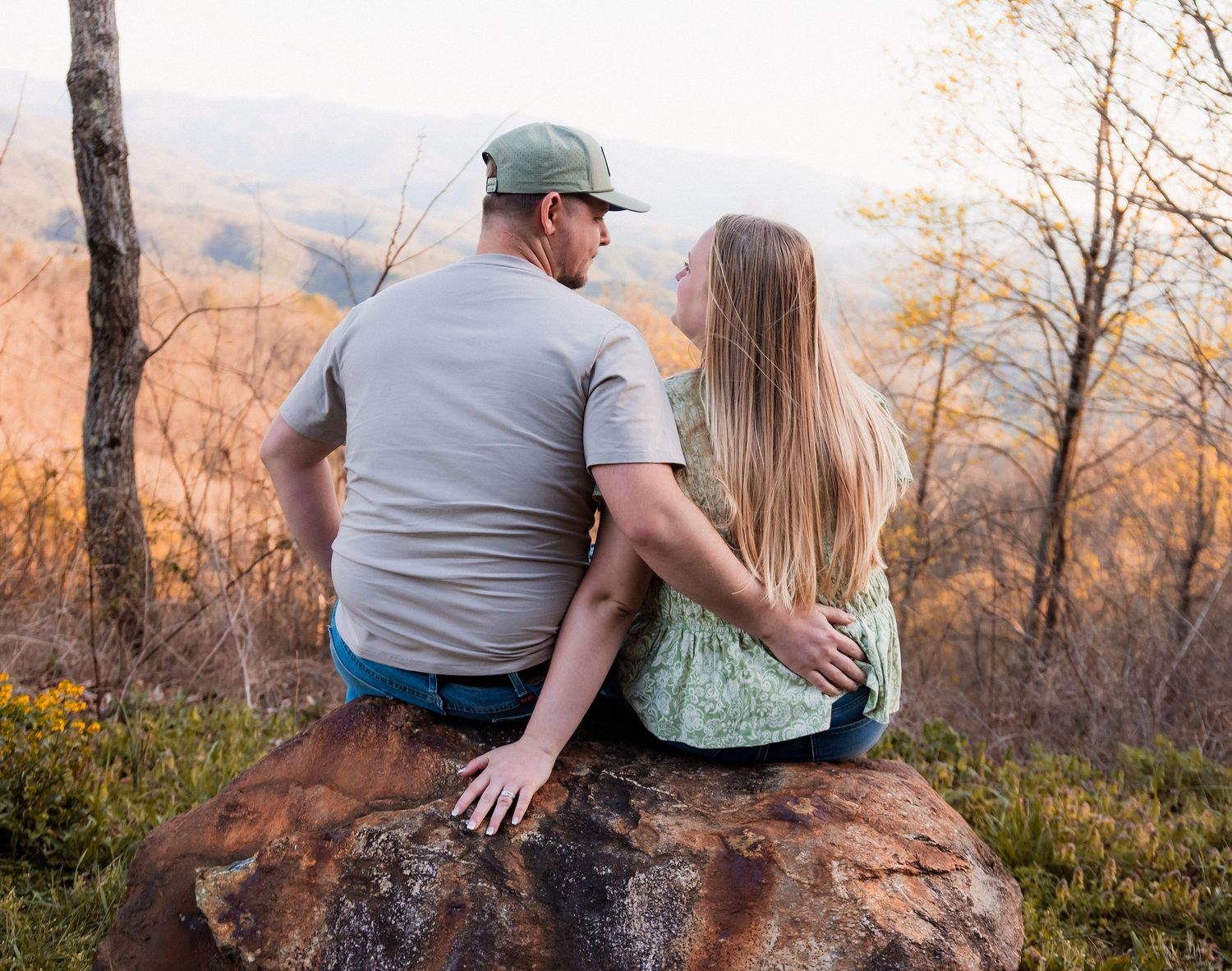 A young couple poses together at a scenic overlook during golden hour with rolling hills in the background.