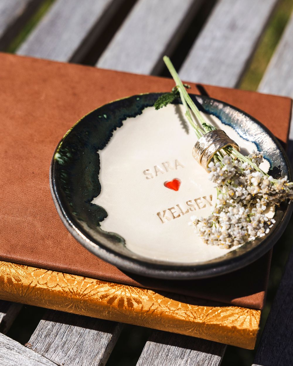 Handmade ceramic ring dish with Sara and Kelsey names and red heart, holding dried lavender and rings.