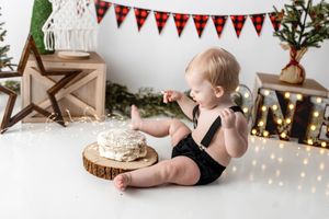 Baby boy in black romper exploring his first birthday cake smash with Christmas holiday decorations.