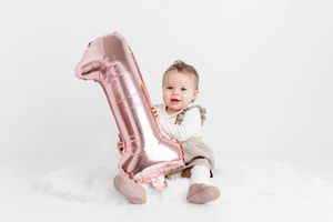 Smiling baby sitting next to a large rose gold number one balloon for first birthday photo session in Menifee.