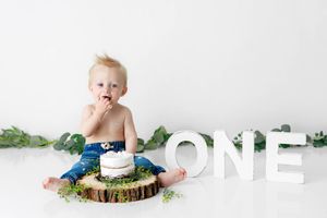 Menifee 1st birthday photographer: Baby boy eats cake beside white ONE letters for first birthday smash session.