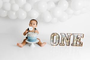 Murrieta 1st birthday photographer: Baby boy in diaper sitting with a blue ombre cake next to a ONE sign and white balloons.