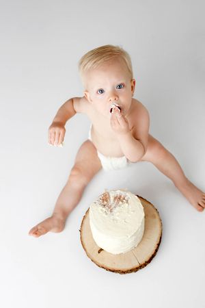 Lake Elsinore 1st birthday photographer: Baby boy  eats cake during first birthday cake smash on white background with wood slice.