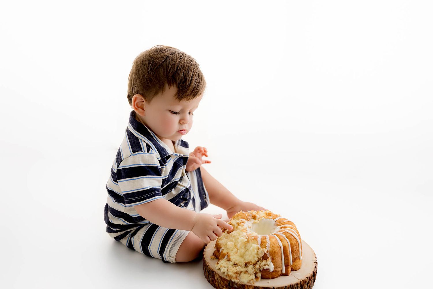 Baby boy eating first birthday smash cake in birthday photoshoot.
