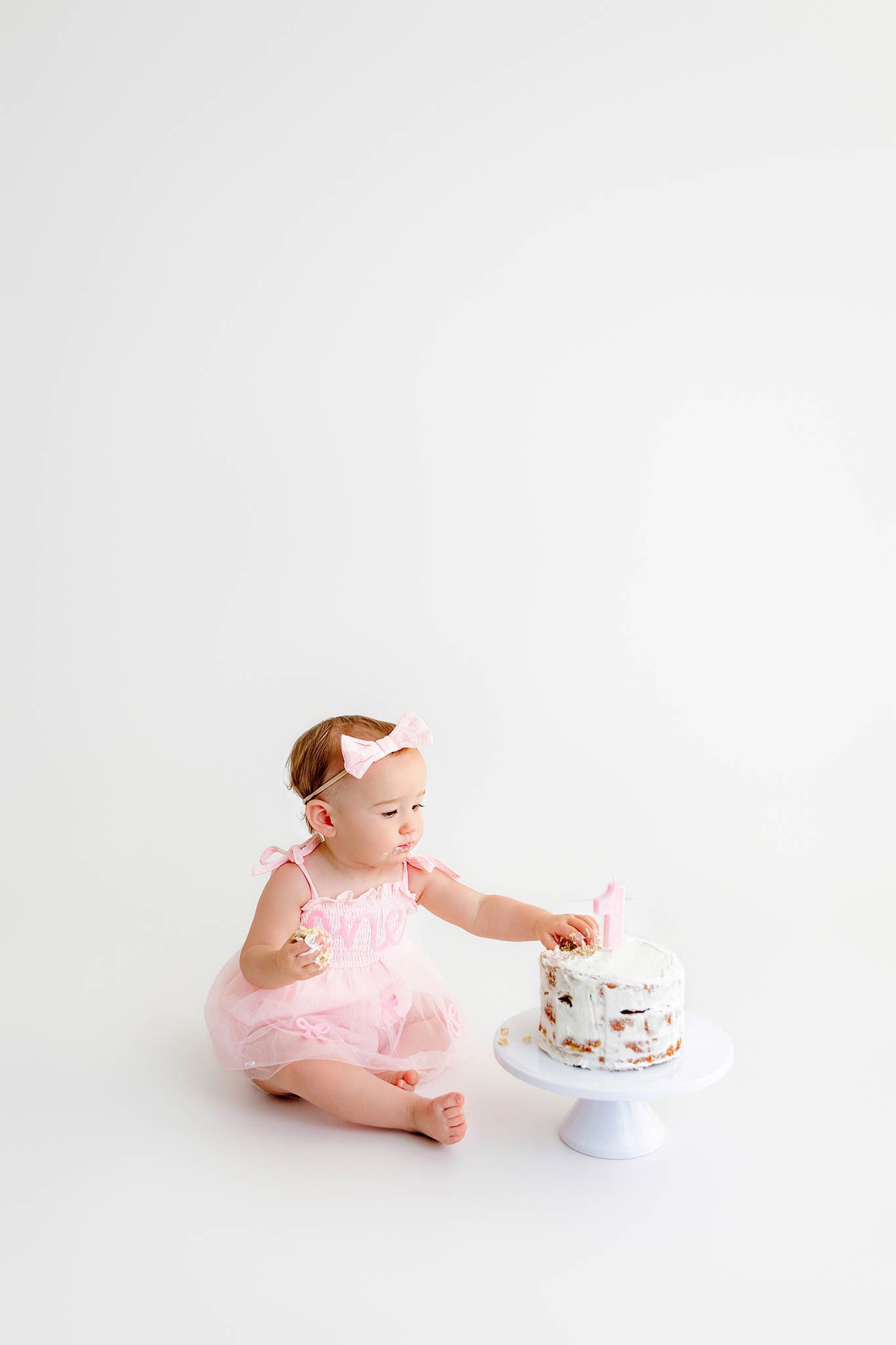 Baby girl in pink tutu dress touches her first birthday cake on white background by Lake Elsinore photographer.