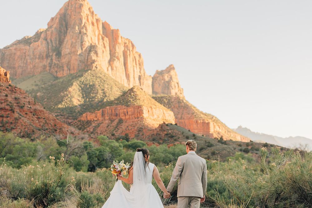 Bride and groom holding hands facing Zion National Park red rock mountains in Utah wedding portrait.