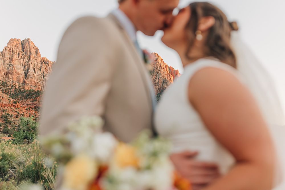 Couple shares romantic kiss with red rock mountains and desert landscape softly blurred in foreground.