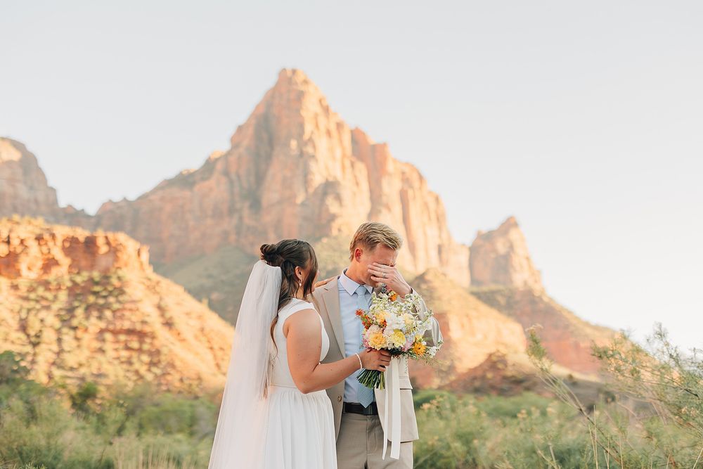 Bride and groom share an intimate moment with colorful bouquet before stunning Zion National Park red rock canyon backdrop.