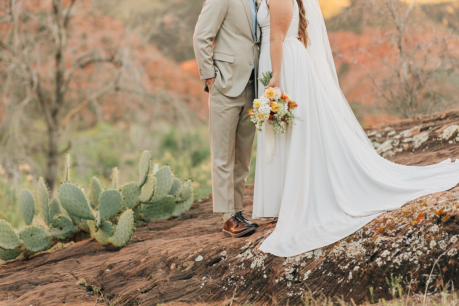 Bride and groom stand on red rock surrounded by desert cacti in Zion National Park wedding.