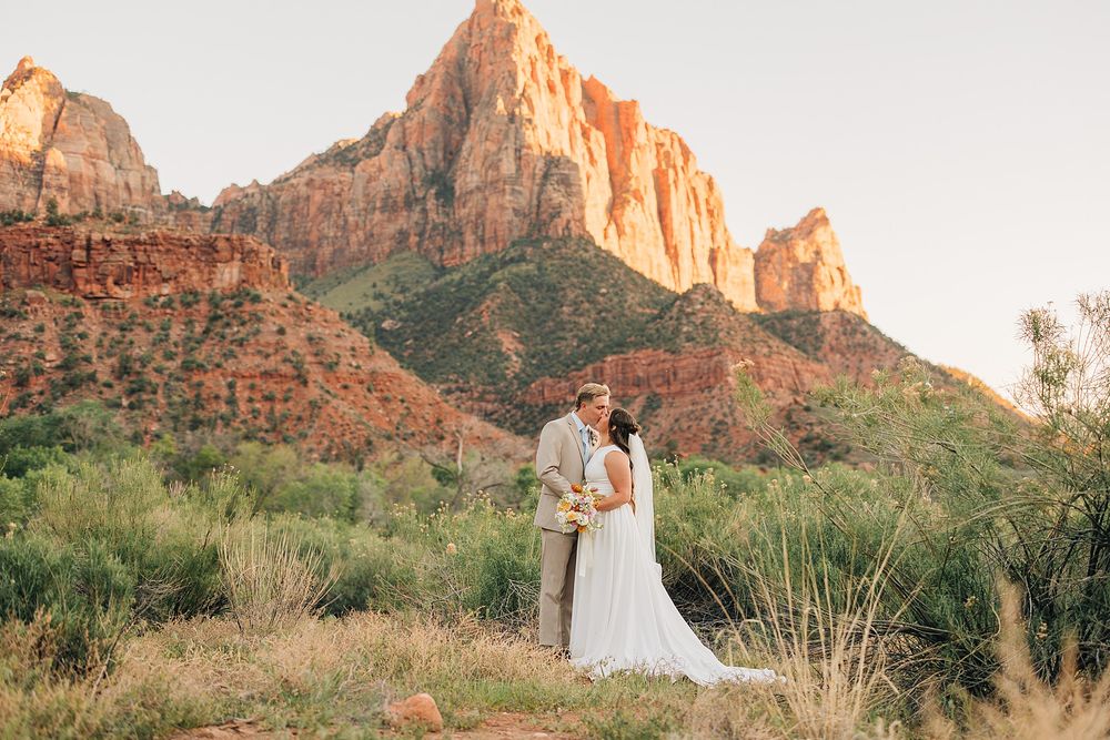 Bride and groom share a romantic kiss at Zion National Park with red rock canyon mountains in the background.