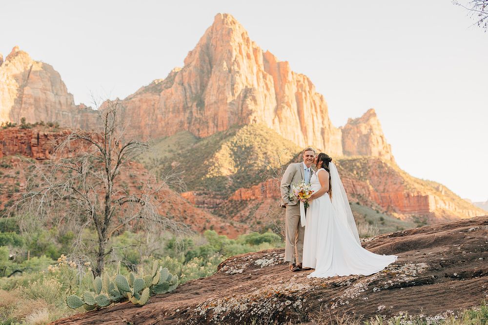 Bride and groom kissing at Zion National Park with The Watchman mountain glowing at sunset.