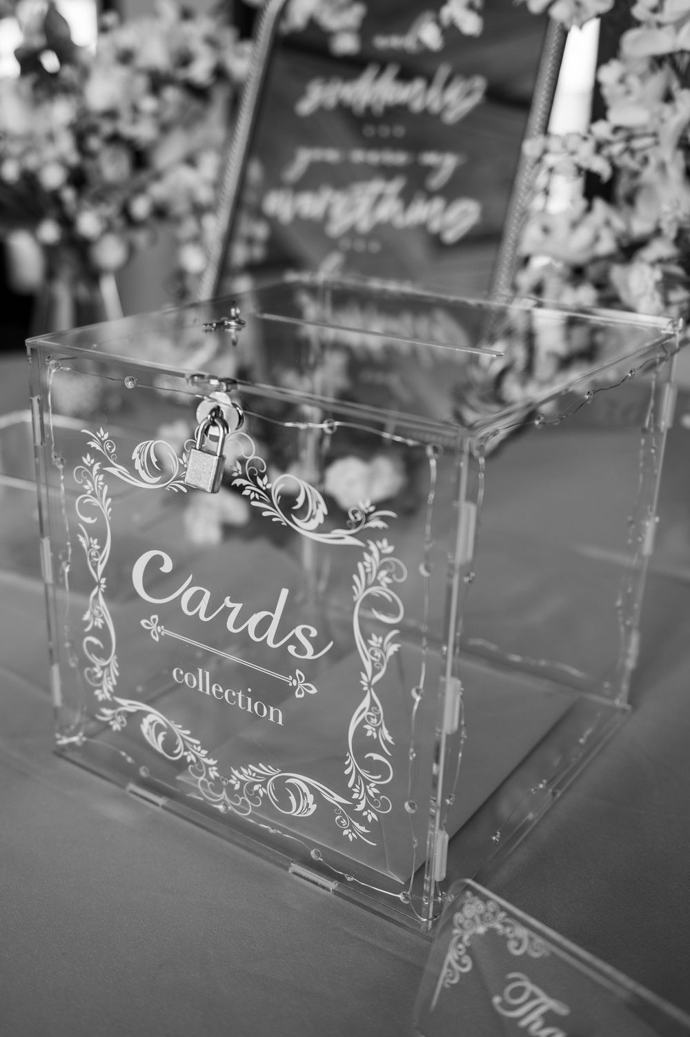 Black and white photo of an elegant acrylic wedding card collection box with ornate engraving and small lock.