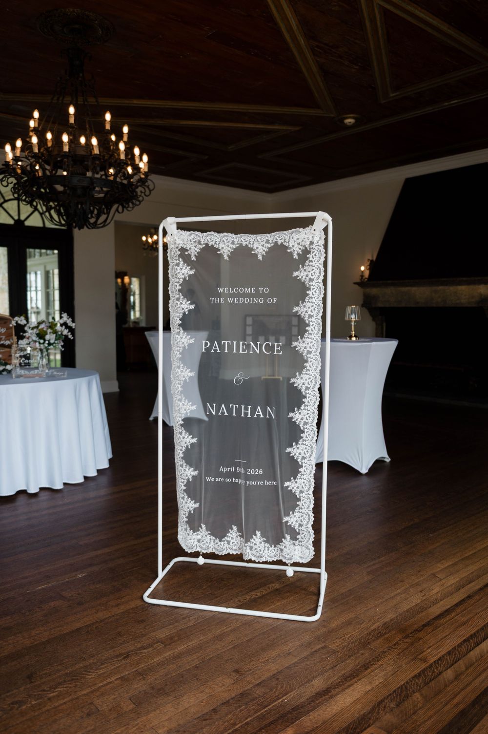 Elegant wedding welcome sign for Patience and Nathan on acrylic display stand in rustic venue with chandelier.