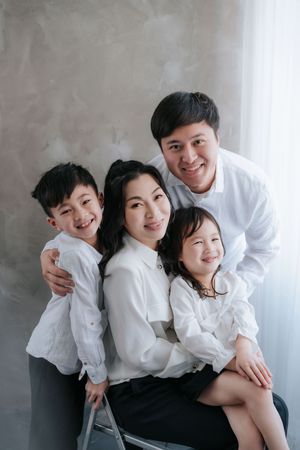 A family wearing white clothes poses together against a gray wall in a series of candid studio portraits在一組自然生動的影棚肖像照中，一家人穿著白色衣服，在灰色牆壁前合影。