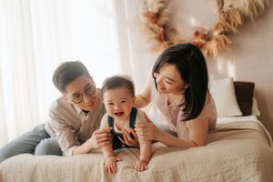 A family plays together and laughs while laying on a white bed in a bright sunlit room.一家人在陽光明媚的房間裡，躺在白色的床上玩耍嬉戲，歡笑聲不斷。