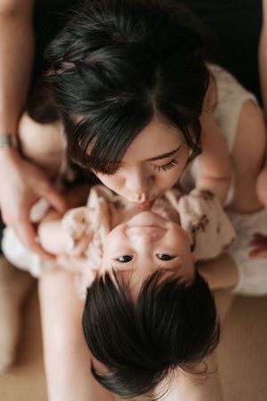 Two people with dark hair in intimate pose lying down and facing each other in soft lighting.兩名黑髮女子在柔和的燈光下，以親密的姿勢躺著，面對面。