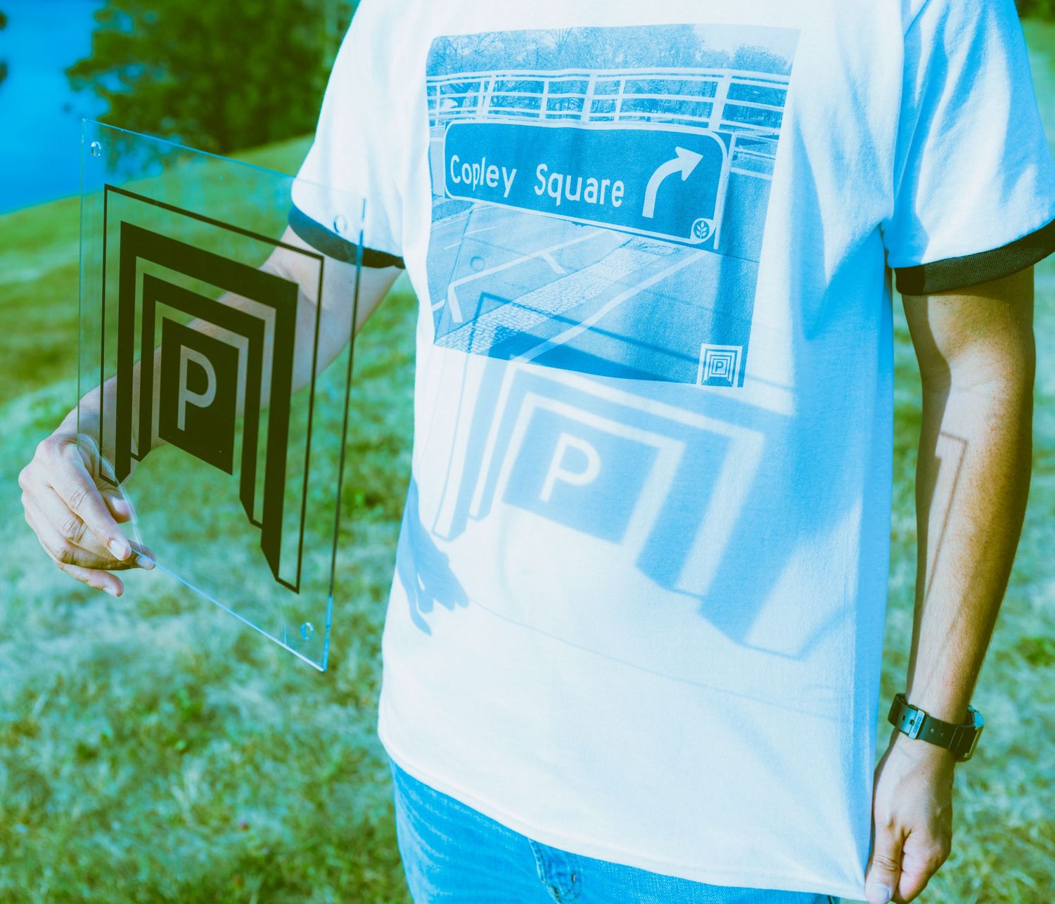 Person holding a parking sign wearing a Copley Square graphic tee shirt outdoors.
